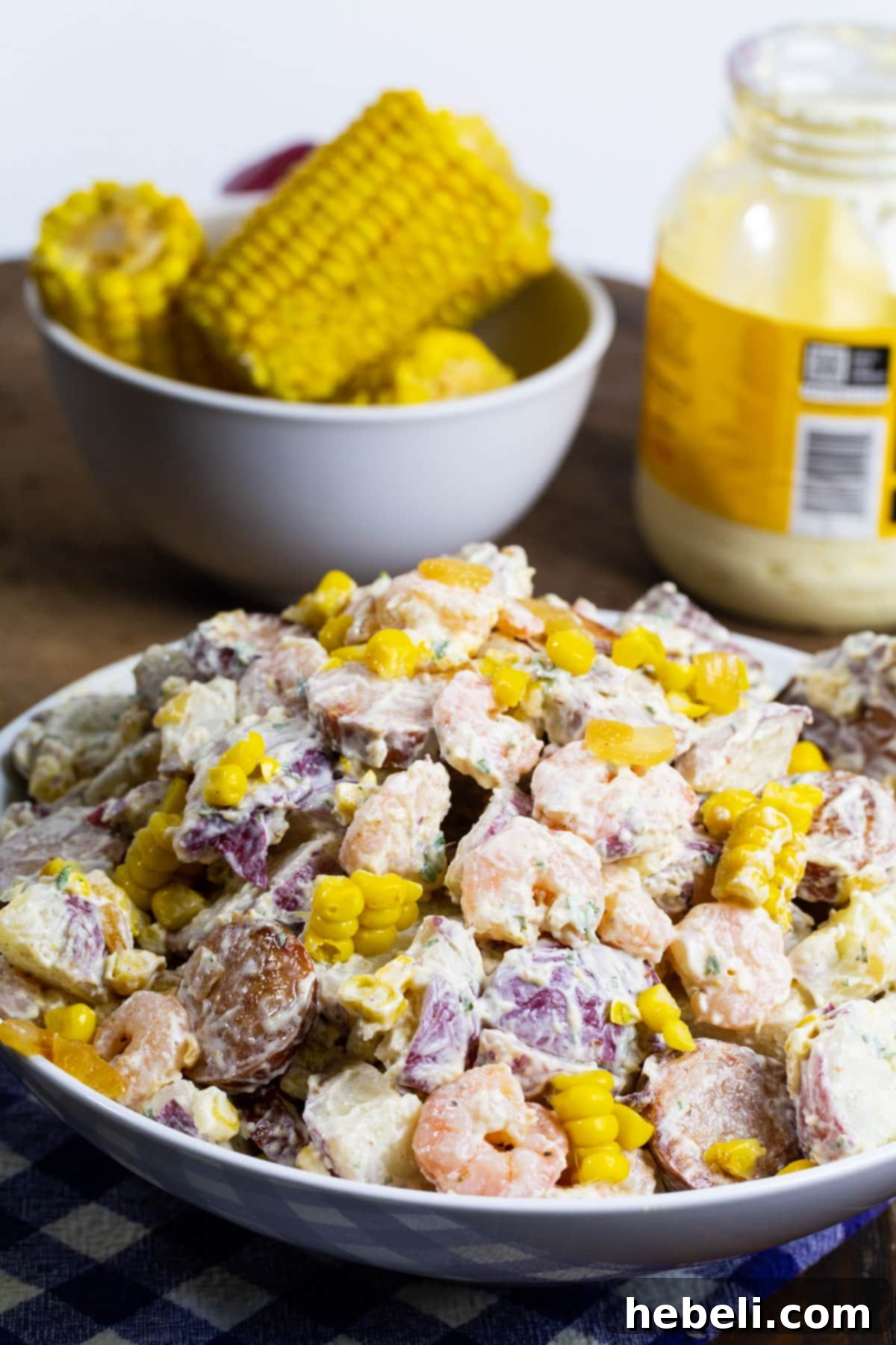 A large serving bowl filled with Frogmore Potato Salad, with fresh corn on the cob visible in the background, set for a summer meal.