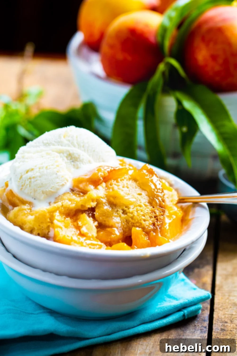 Set-It-and-Forget-It Peach Cobbler 3 A cozy bowl of Slow Cooker Peach Cobbler with melting vanilla ice cream, set against a blurred background of fresh peaches, highlighting its homemade appeal.