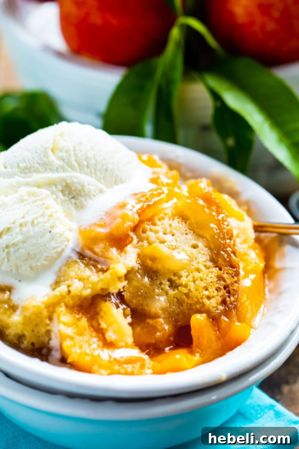 Set-It-and-Forget-It Peach Cobbler 4 A close-up of a delightful Slow Cooker Peach Cobbler served in a white bowl, generously topped with creamy vanilla ice cream, ready to be enjoyed as a sweet treat.