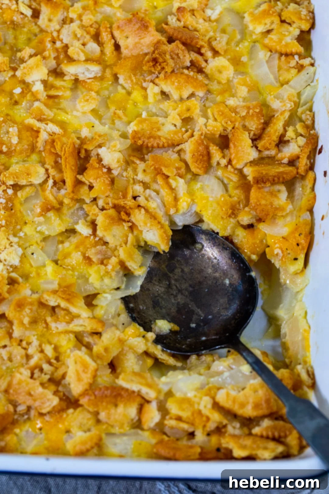 Spoon scooping up Vidalia Onion Casserole with Ritz cracker topping, showing texture.