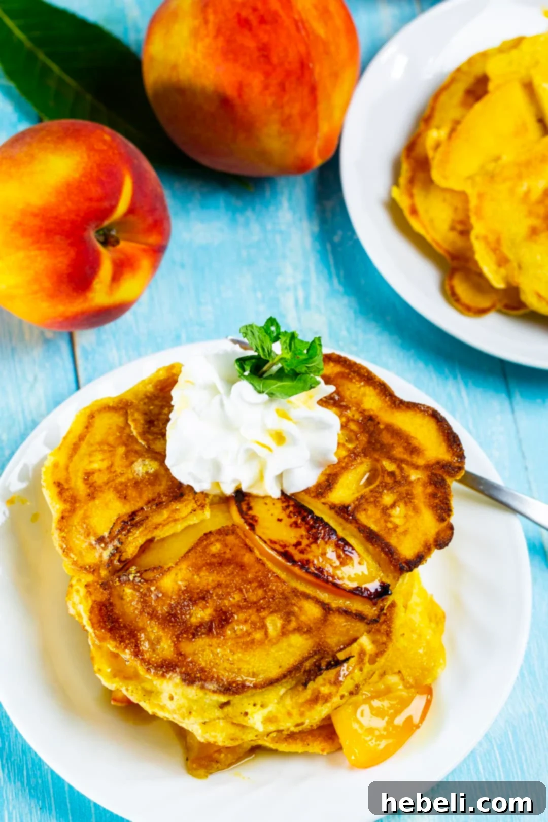 A stack of golden Sweet Peach Pancakes nestled on a plate, surrounded by fresh peach slices.