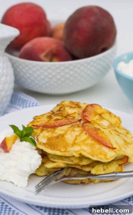 Close-up of a stack of golden Sweet Peach Pancakes, with vibrant fresh peach slices elegantly arranged in the background.
