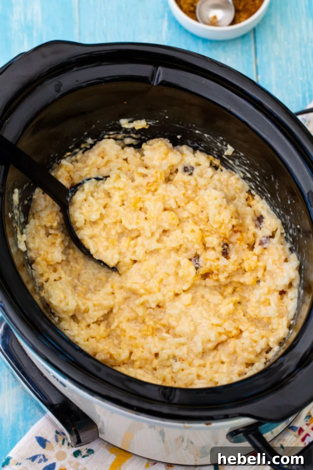 Slow Cooker Rice Pudding being gently stirred, showing off its developing creamy consistency.