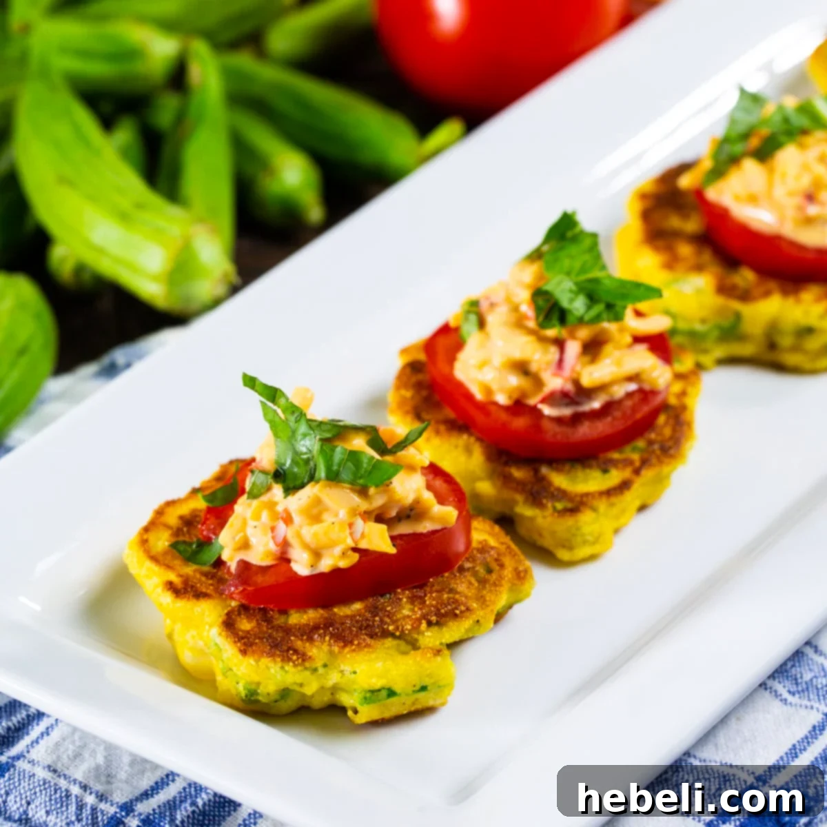 Golden brown Okra Pancakes with Pimento Cheese, garnished with fresh tomato and basil, arranged on a rustic serving plate.