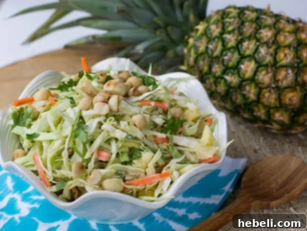 Pineapple Macadamia Slaw in a white bowl with a whole pineapple in the background.