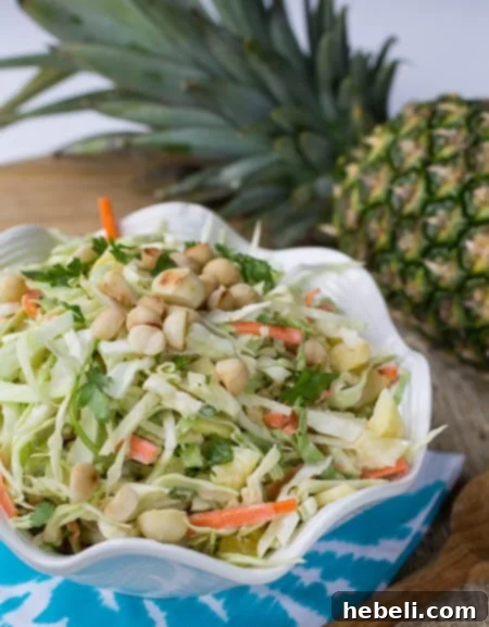 Pineapple Macadamia Slaw in a white serving bowl with a whole pineapple in the background.