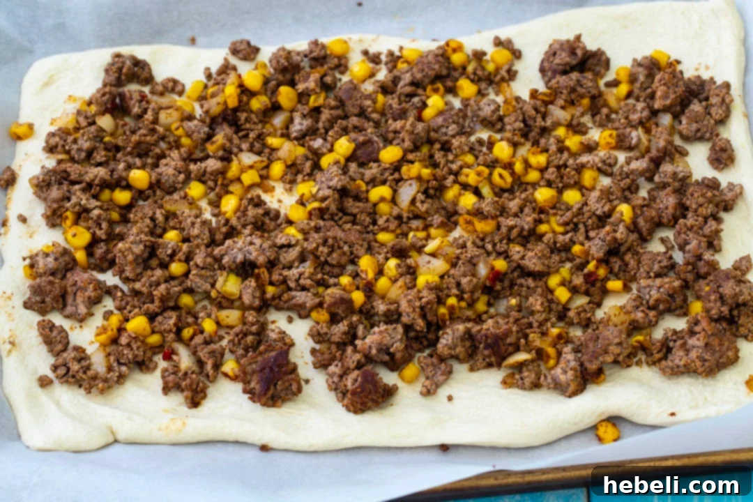 Fiesta Pizza Rolls 3 Taco filling made with seasoned ground beef and corn spread evenly over a rolled-out pizza dough.