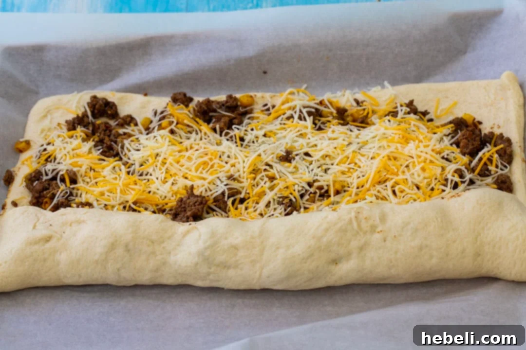 Fiesta Pizza Rolls 4 Refrigerated pizza dough being carefully rolled up with the taco filling inside to form a log.