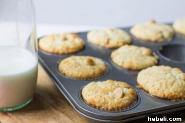 Freshly baked muffins cooling in a muffin tin, with a jar of milk in the background, suggesting a delightful pairing.