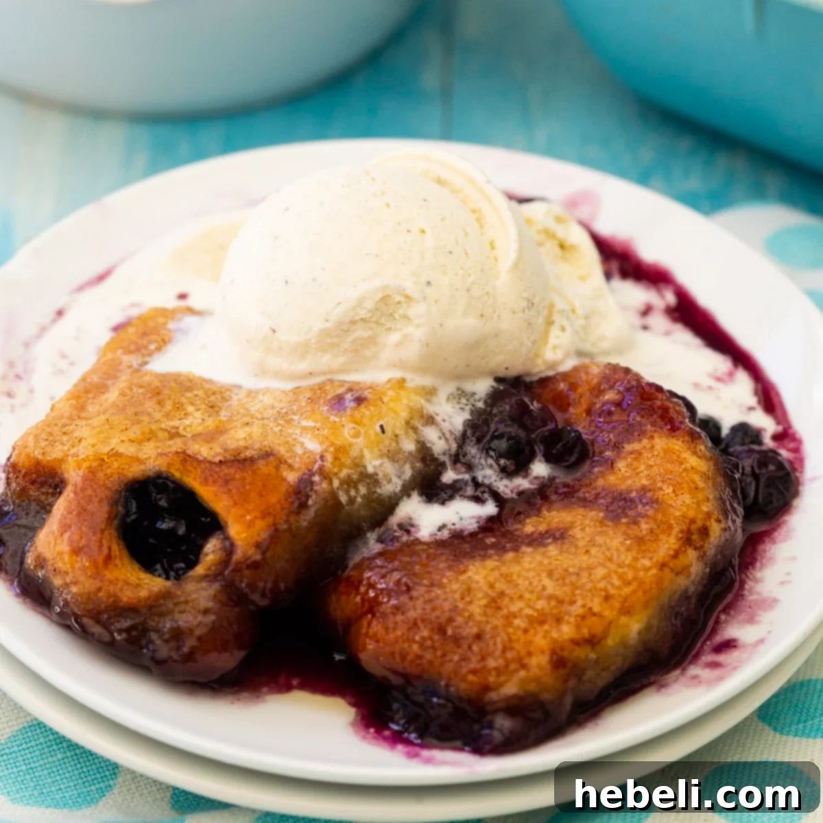 Golden brown blueberry dumplings topped with a scoop of melting vanilla ice cream, served in a white bowl.
