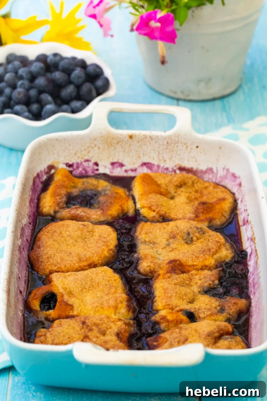 Freshly baked blueberry dumplings in a rectangular glass baking dish, showing a golden crust and bubbling sauce.