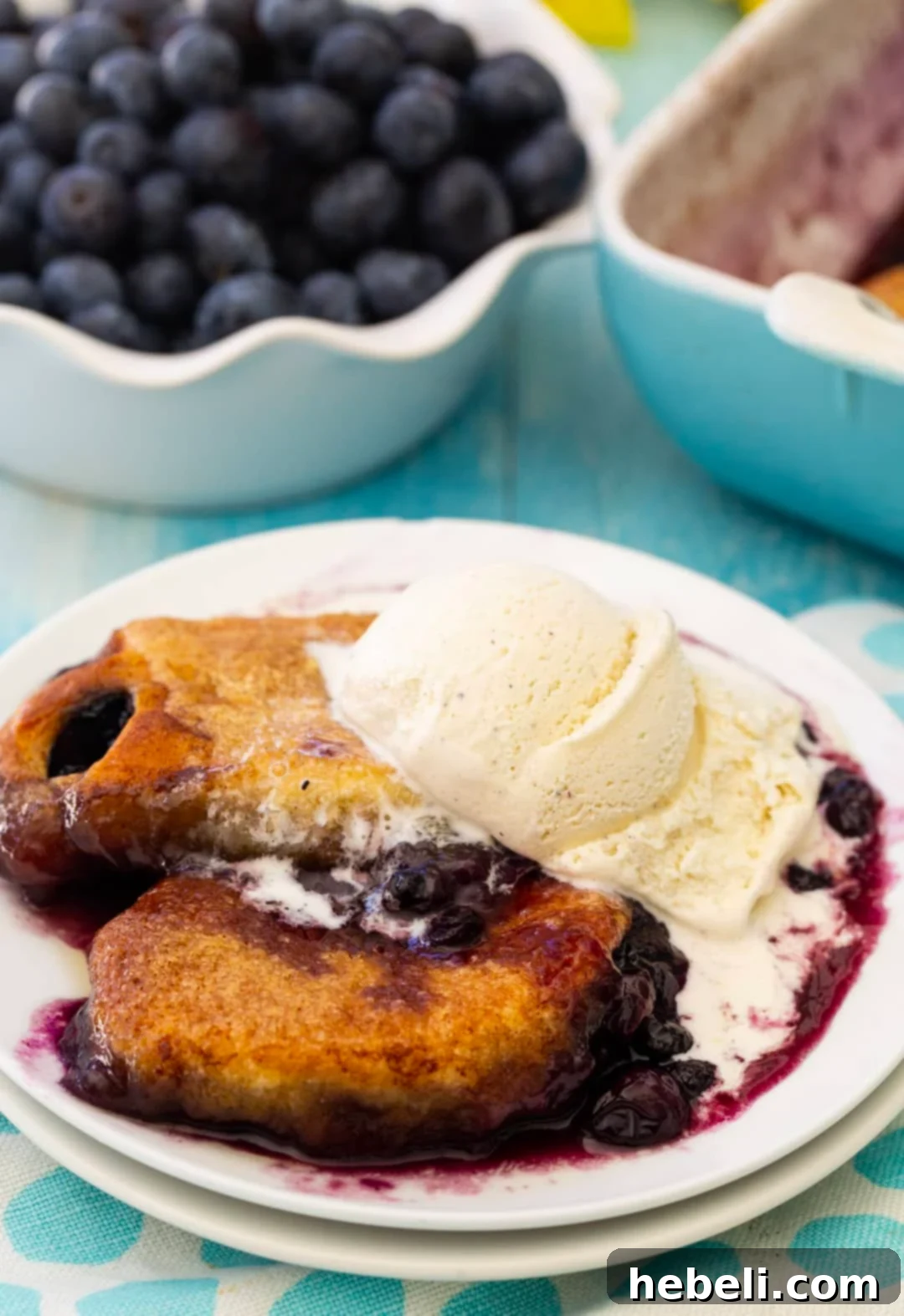 Close-up of warm blueberry dumplings with a scoop of melting vanilla ice cream in a white serving bowl.
