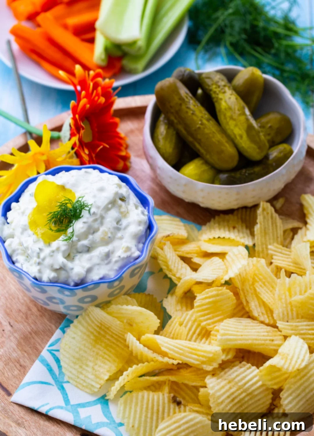 Close-up shot of creamy Dill Pickle Dip in a rustic ceramic bowl, with a variety of serving options like potato chips and vegetable sticks surrounding it.
