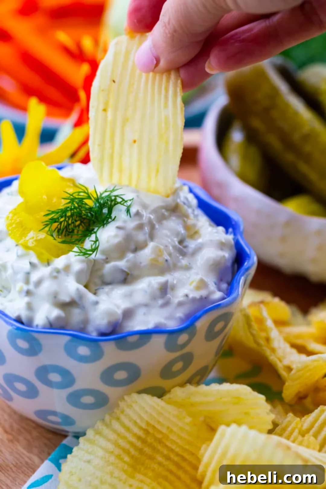 A hand dipping a crispy potato chip into a bowl of creamy Dill Pickle Dip, highlighting its perfect consistency and tempting texture.