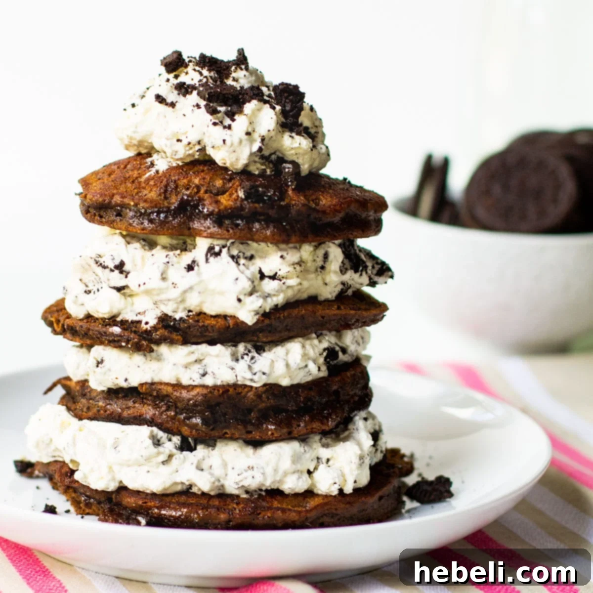 Stack of fluffy Double Stuffed Oreo Pancakes on a plate, layered with creamy white Oreo whipped cream, ready to be enjoyed.