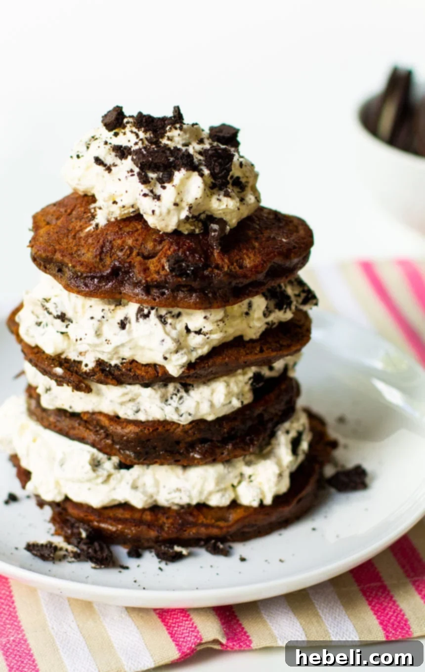 Close-up of a stack of Double Stuffed Oreo Pancakes topped with a dollop of Oreo whipped cream and more crushed Oreos.