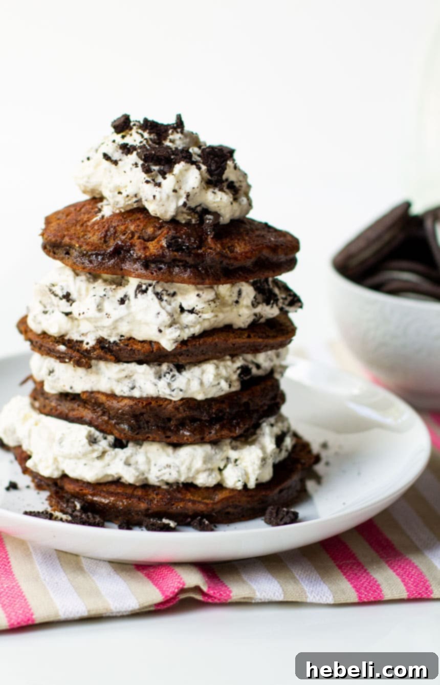 Side view of Double Stuffed Oreo Pancakes stacked on a white plate, showcasing the thick layers of cream filling.