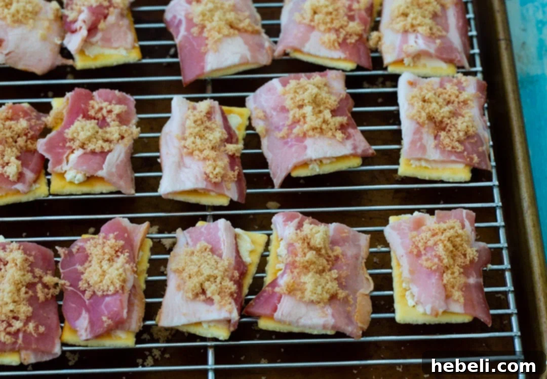 Bacon Boursin Cracker Bites 6 Unbaked Boursin Bacon Crackers meticulously arranged on a wire rack over a baking sheet, sprinkled with a sweet and spicy brown sugar mixture, ready to be placed into the oven.
