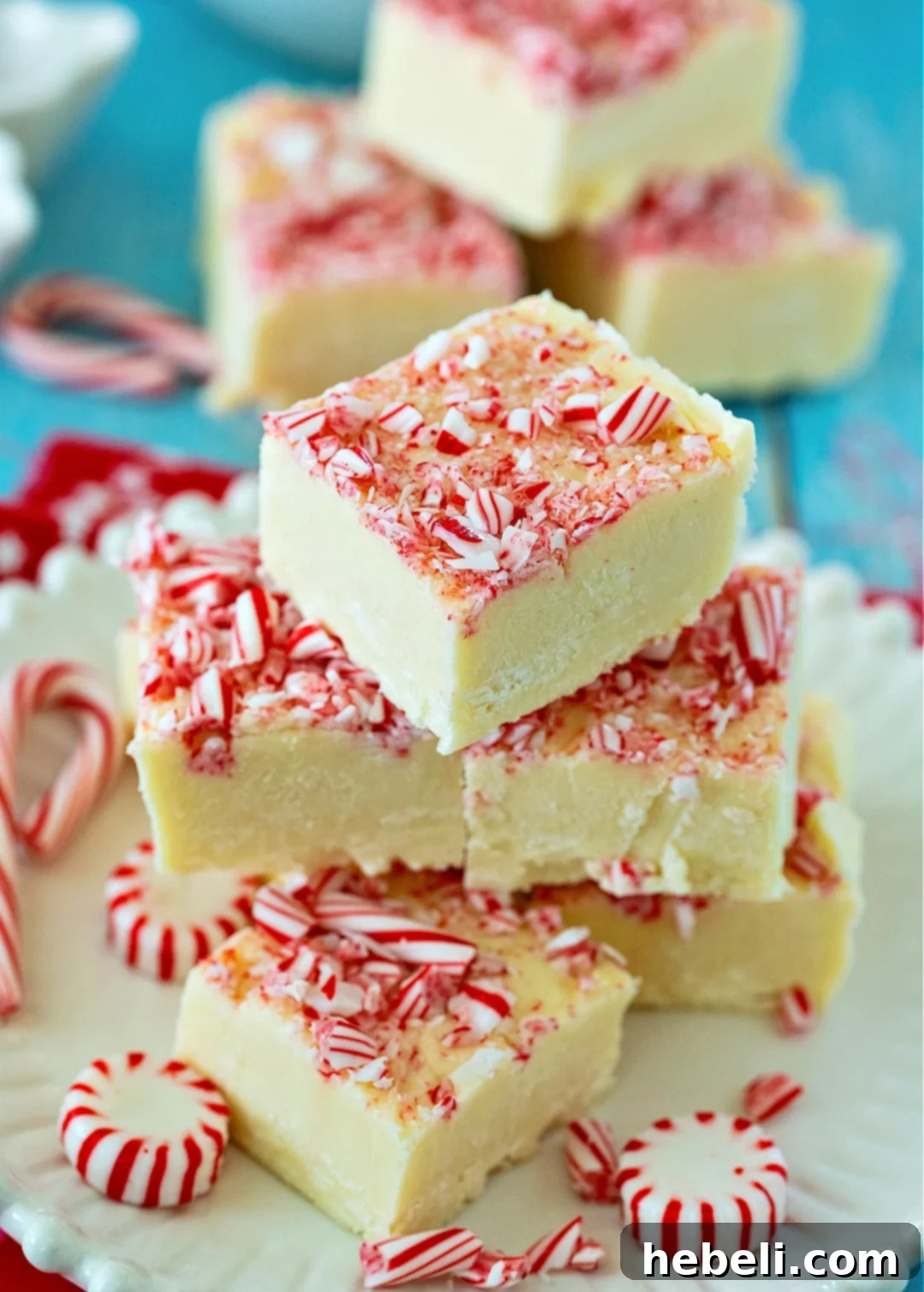 Peppermint Cloud Fudge 4 A close-up of a stack of Peppermint White Chocolate Fudge squares, showcasing their creamy texture and festive candy cane topping.
