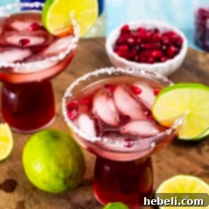 A close-up of a Pomegranate Margarita glass with a fresh lime garnish, embodying the spirit of this recipe.