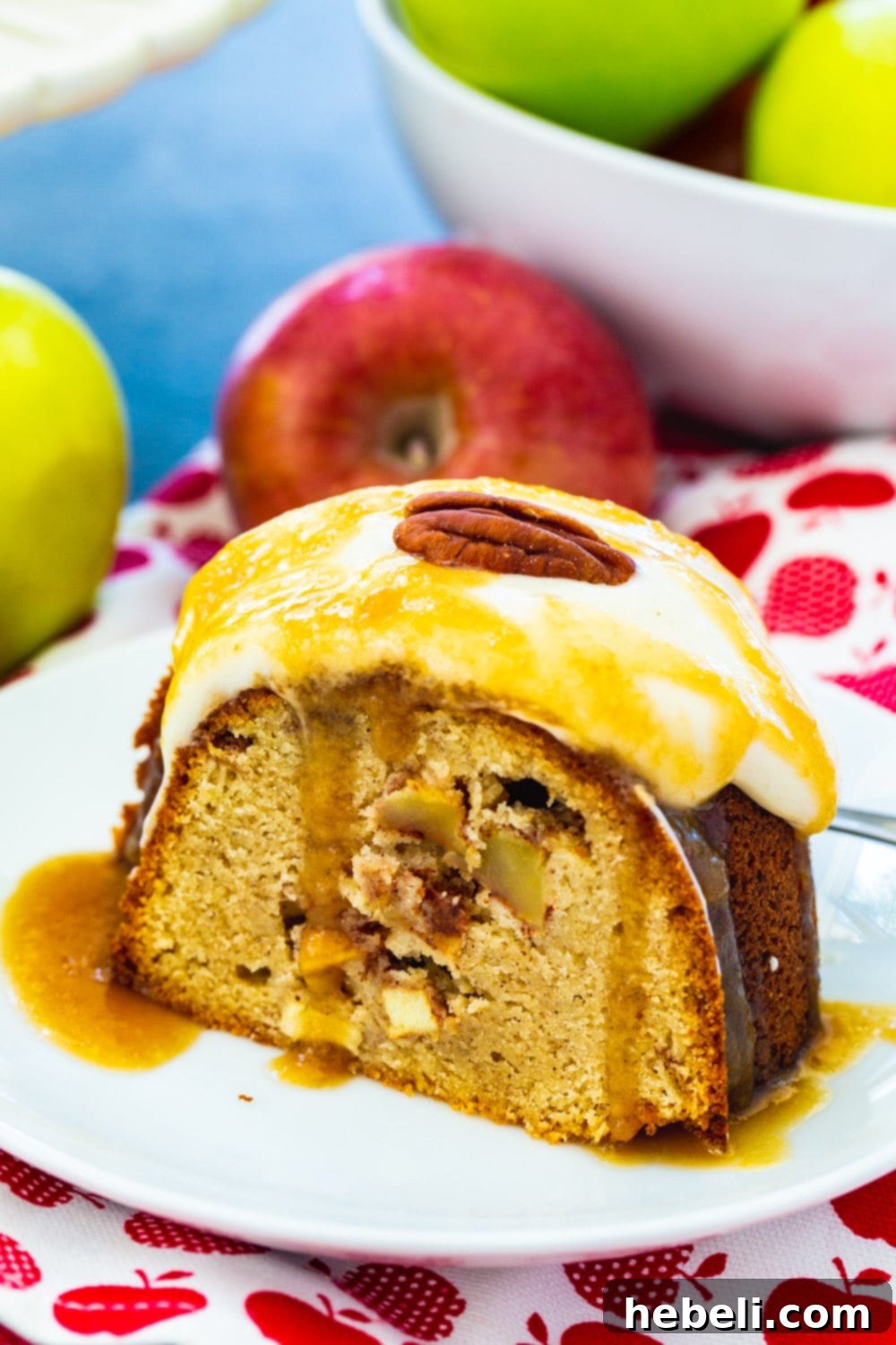 A perfect slice of Caramel Apple Pound Cake served on a small white plate, with fresh red and green apples artfully arranged in the background, highlighting its autumnal appeal.