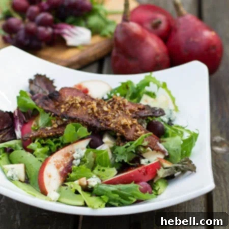 Close-up of a rustic white bowl brimming with Apple and Pear Salad, prominently featuring slices of golden Maple-Pecan Bacon and fresh greens.
