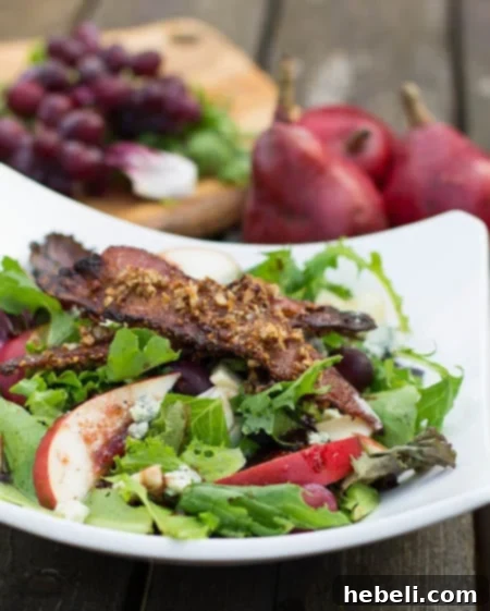 A beautifully composed fall salad, featuring vibrant sliced apples, succulent pears, sweet grapes, and rich Gorgonzola cheese. The background highlights red pears and grapes, creating an inviting seasonal tableau.