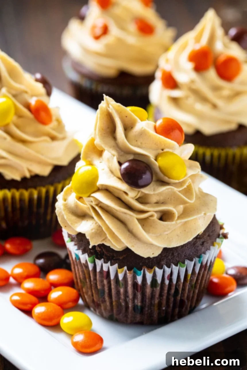 Cupcakes topped with vibrant peanut butter frosting and Reese's Pieces on a plate.