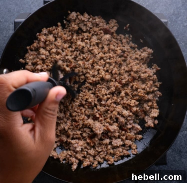 Cooked and crumbled sausage in a skillet, ready for flour.