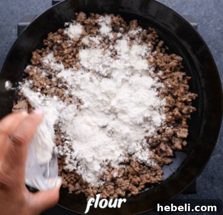 Flour added to cooked sausage in skillet, being stirred to make a roux.