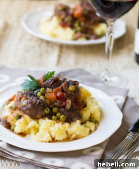 Effortless Slow Cooker Provencal Beef Daube 3 A serving of Slow Cooker Beef Daube Provencal on mashed potatoes, accompanied by a glass of red wine, ready to be enjoyed.