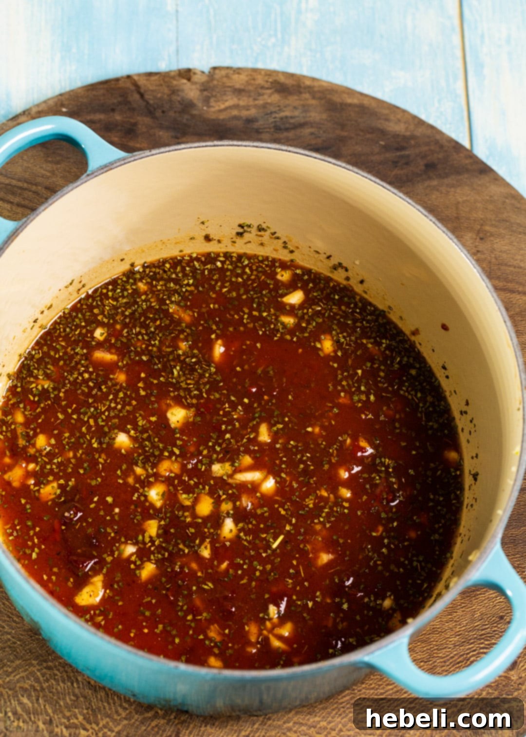 Ketchup, chipotle peppers in adobo sauce, and various spices being stirred together in a Dutch oven to form the flavorful base for the beef.