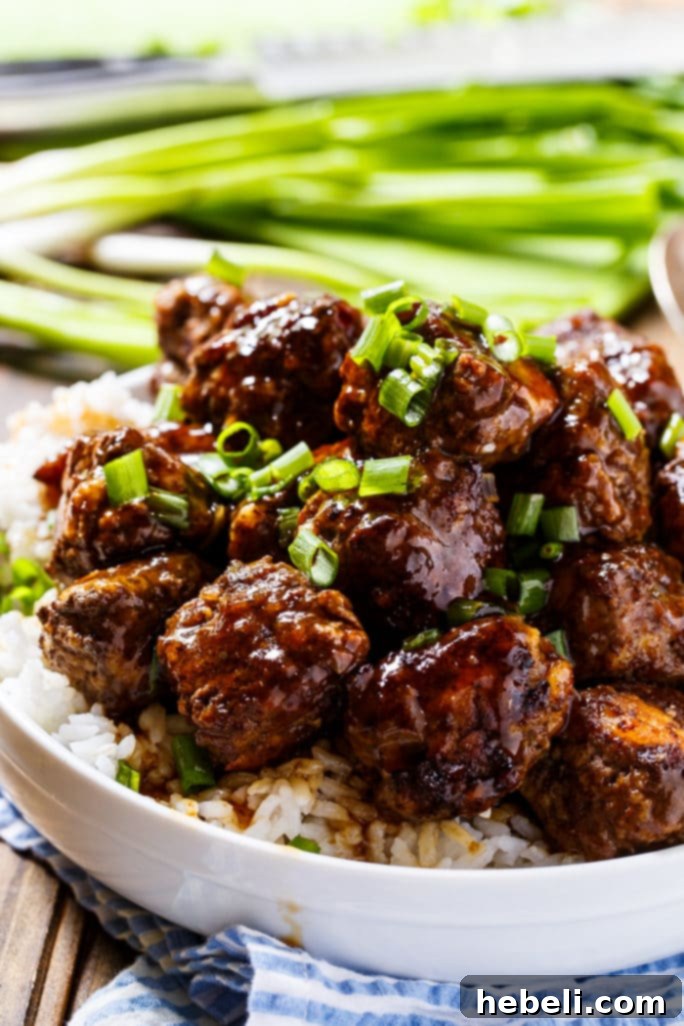 Fiery Apple Glaze Meatballs 3 Close-up shot of glossy, glazed meatballs served over white rice in a bowl, with blurred green onions in the background.