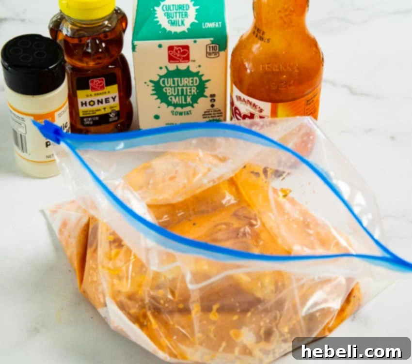 Ingredients for buffalo honey chicken thighs, including buttermilk, buffalo sauce, honey, and chicken in a marinating bag.
