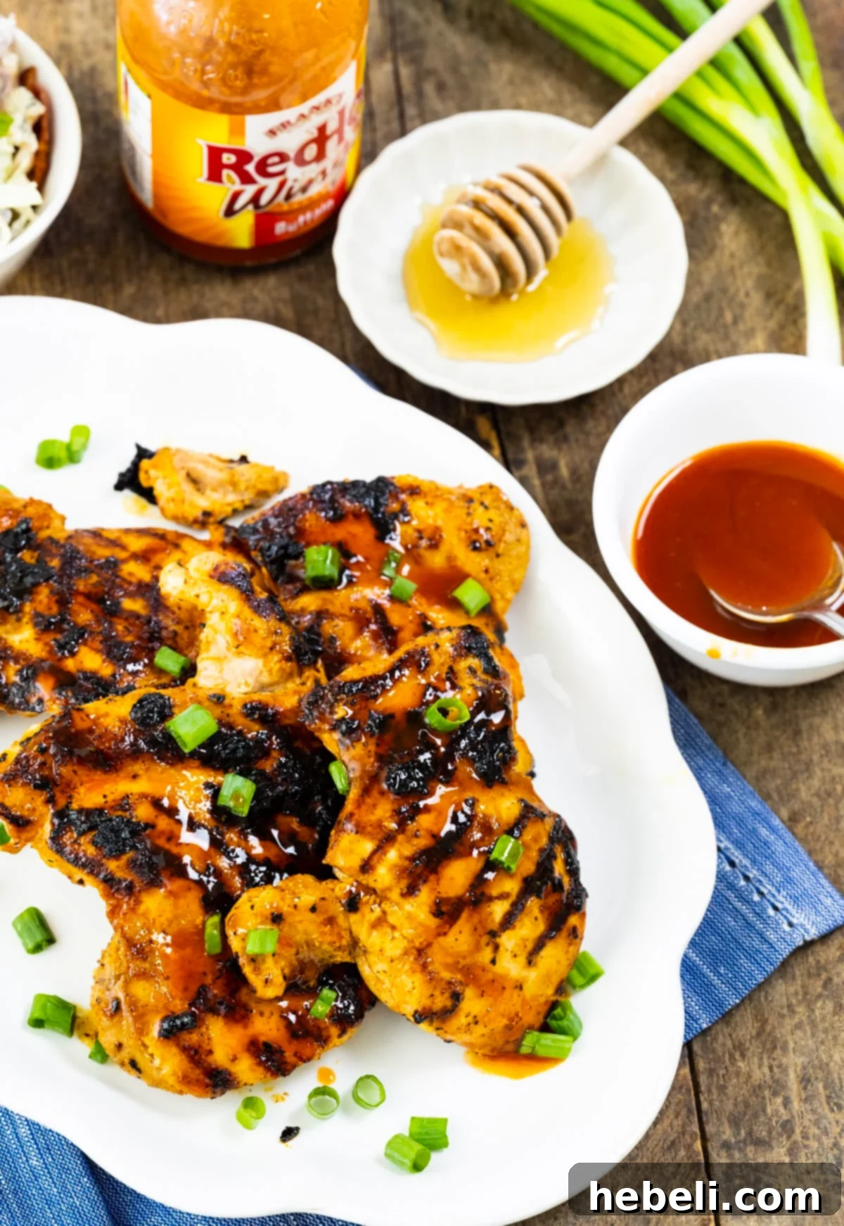 Grilled chicken thighs on a serving platter with a bowl of honey buffalo glaze on the side.