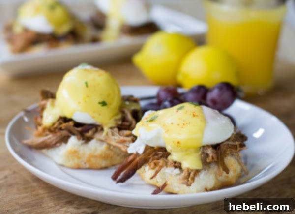 Eggs Benedict on a white plate with red grapes beside it.