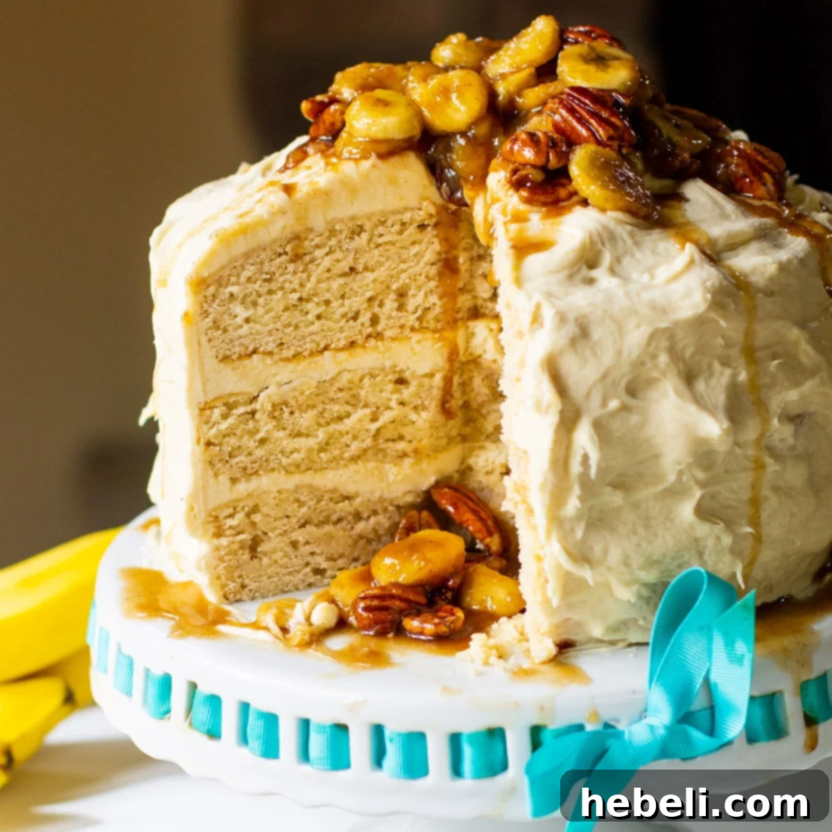 Three-layer Bananas Foster Cake topped with caramelized bananas and pecans, served on an elegant cake stand.