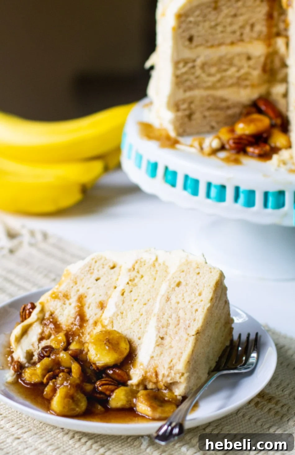 A delicious slice of Bananas Foster Cake on a white plate, showcasing the layered cake, frosting, and banana topping.