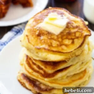 Stack of fluffy buttermilk pancakes on a white plate, topped with a pat of butter.