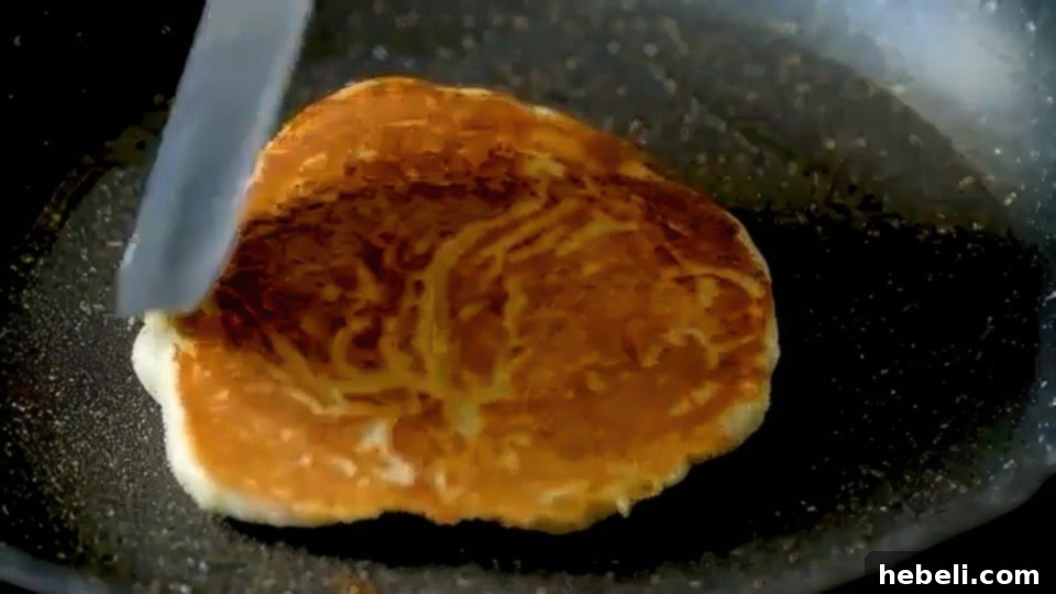 Fluffy Buttermilk Pancakes 7 A pancake cooking in a skillet, showing bubbles forming on its surface before flipping.