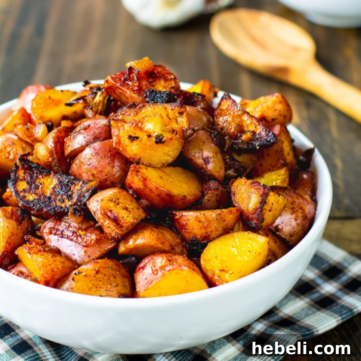 A rustic white bowl overflowing with beautifully cooked, reddish-brown paprika potatoes, garnished with fresh parsley.