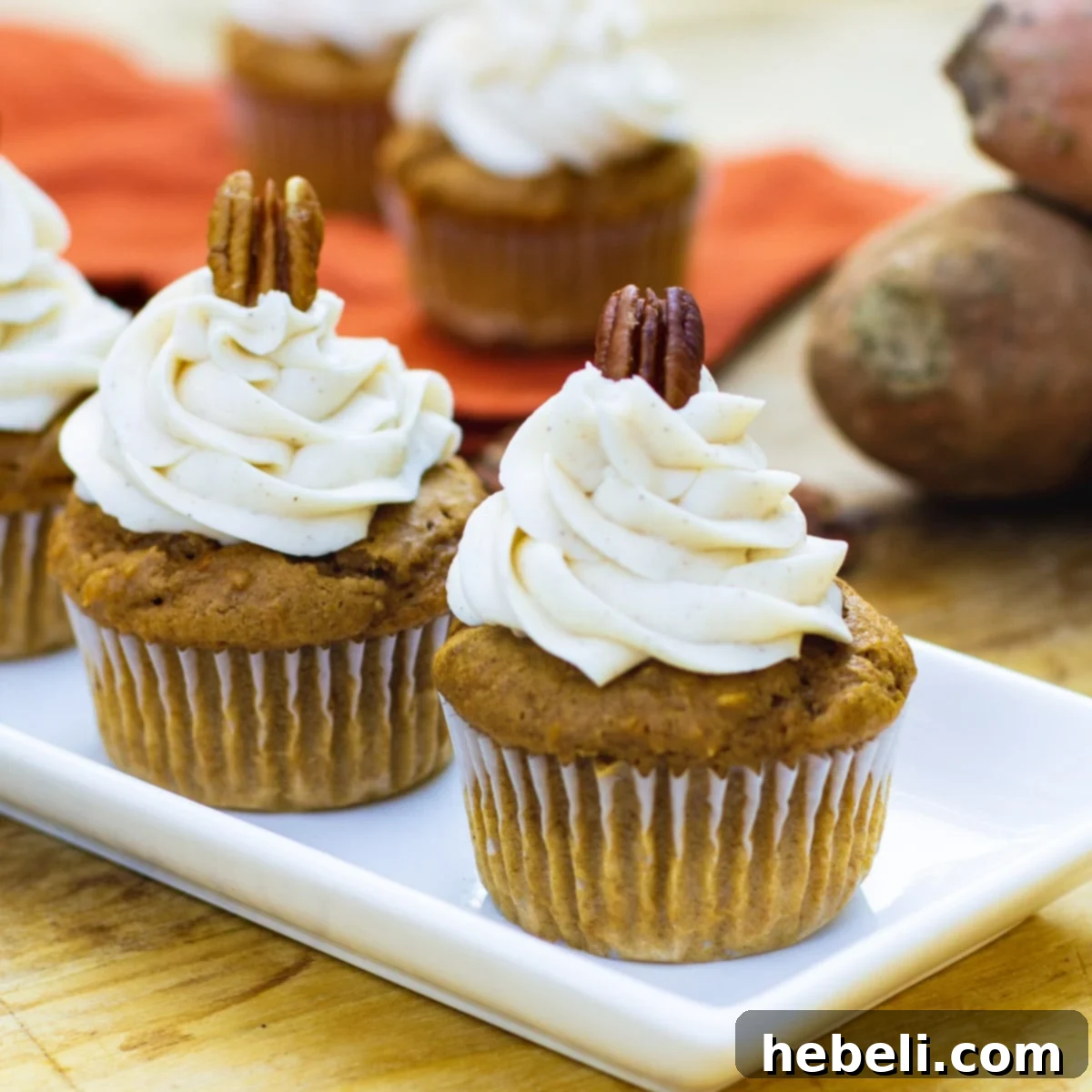 Delicious Sweet Potato Cupcakes with Spiced Buttercream on a serving tray, with fresh sweet potatoes in the background, perfect for a fall dessert.