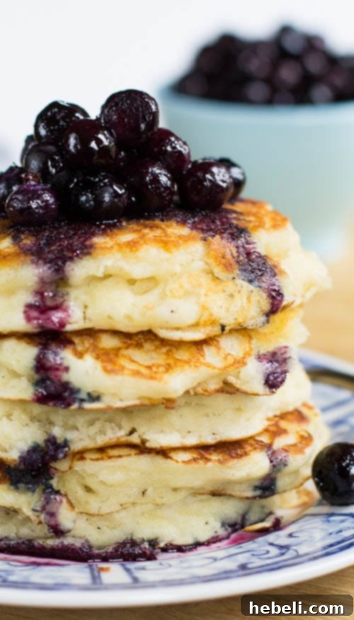 A tall stack of fluffy buttermilk pancakes with blueberry compote, garnished with fresh blueberries.