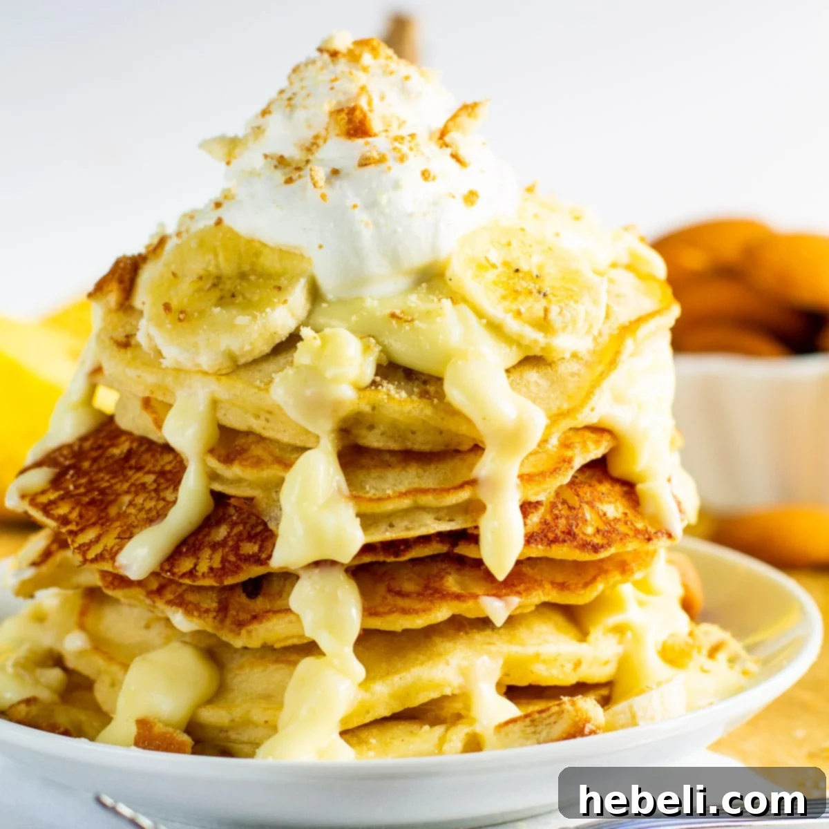 Decadent Banana Pudding Pancakes 2 Stack of fluffy Banana Pudding Pancakes layered with creamy pudding sauce, fresh banana slices, and topped with whipped cream and crushed vanilla wafers.
