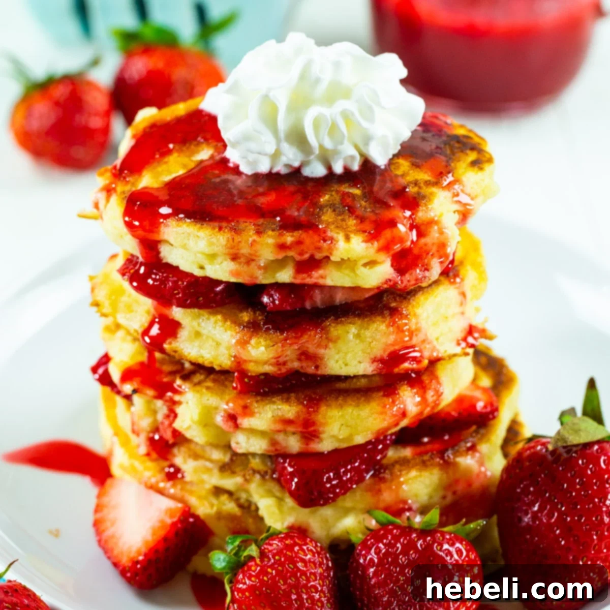 Stack of Strawberry Shortcake Pancakes topped with whipped cream and fresh strawberries, ready to be served.