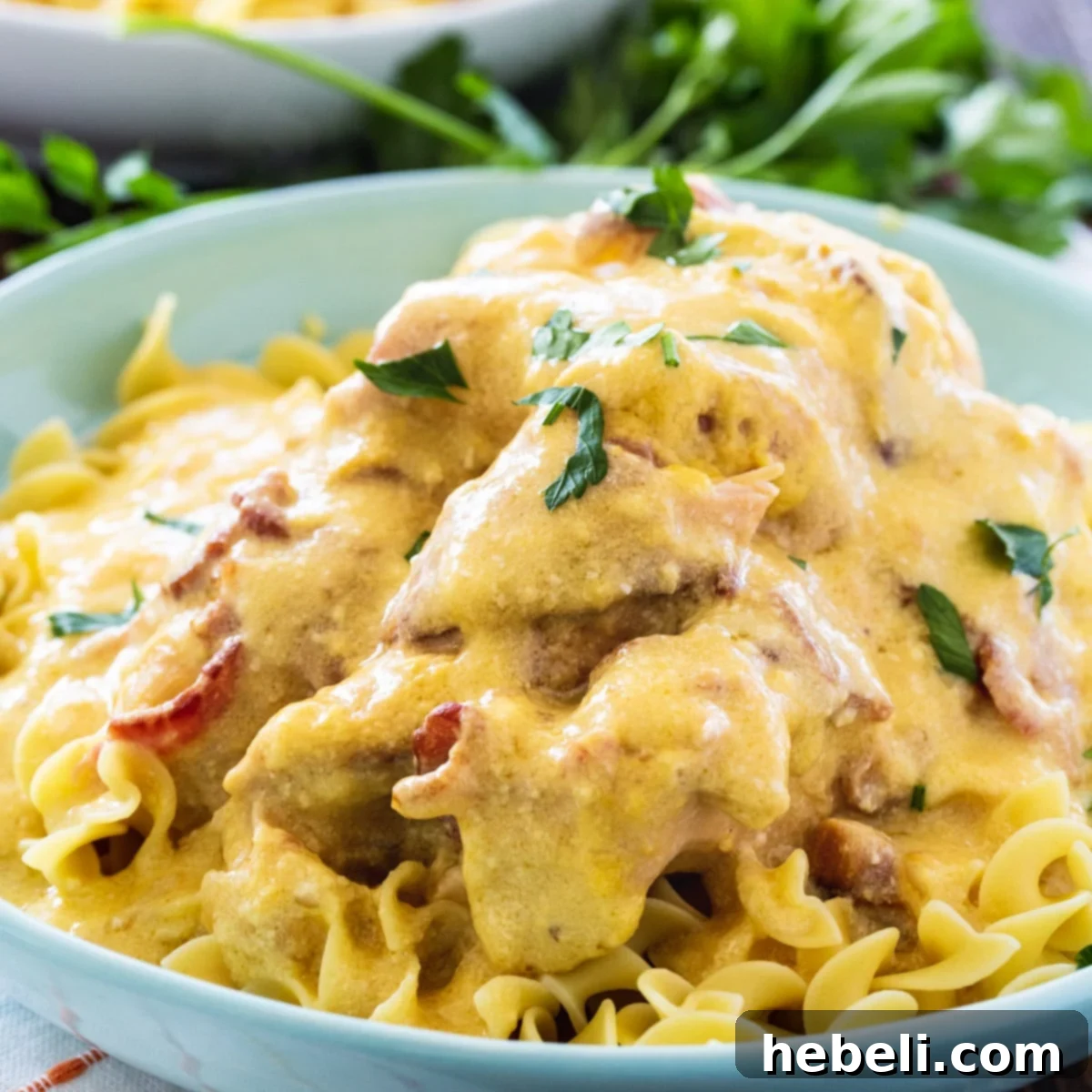 Sour Cream and Bacon Chicken over noodles in a bowl, showcasing the rich, creamy sauce and tender chicken.