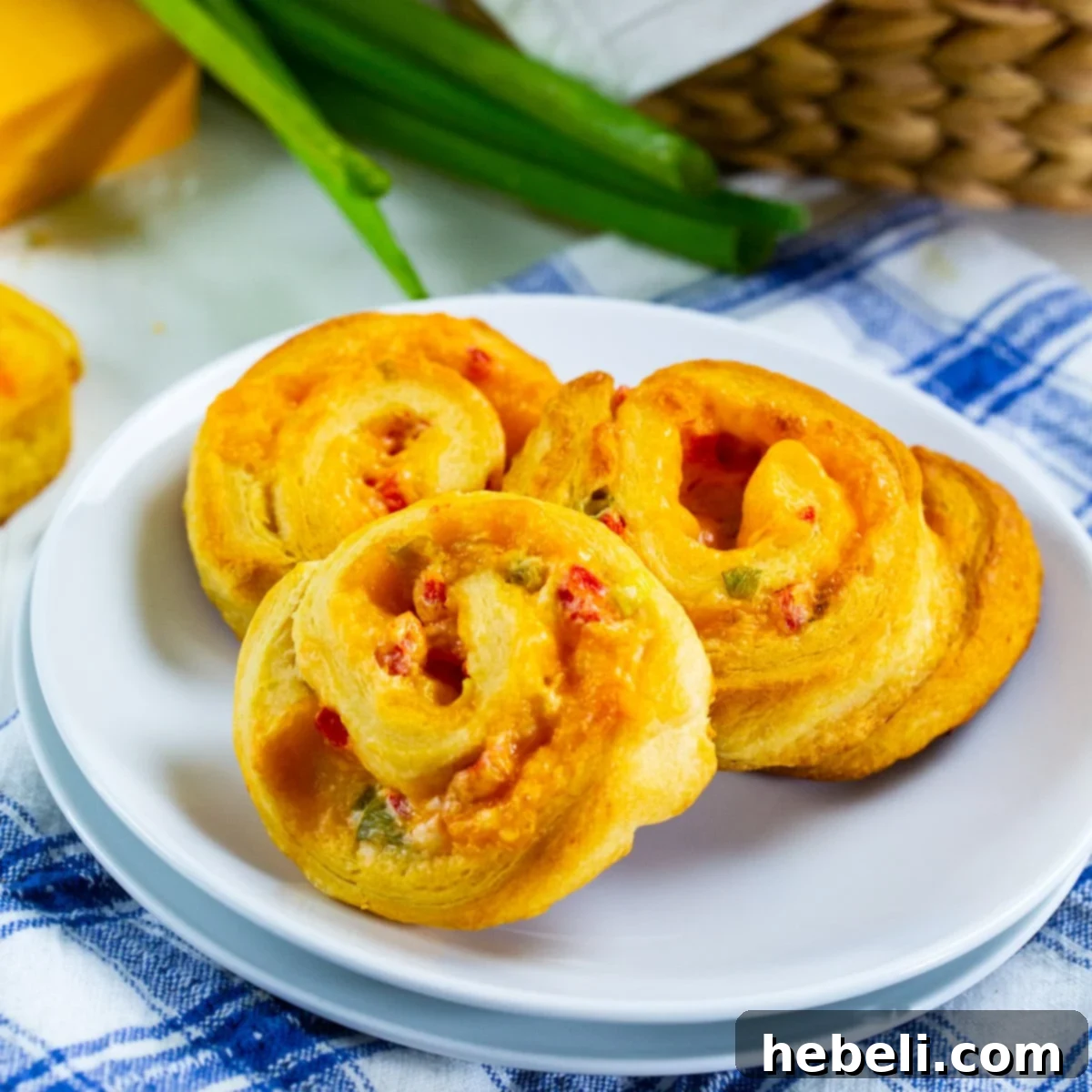 Three golden brown Pimiento Cheese Spirals on a white plate, showcasing their cheesy filling and perfect swirl.