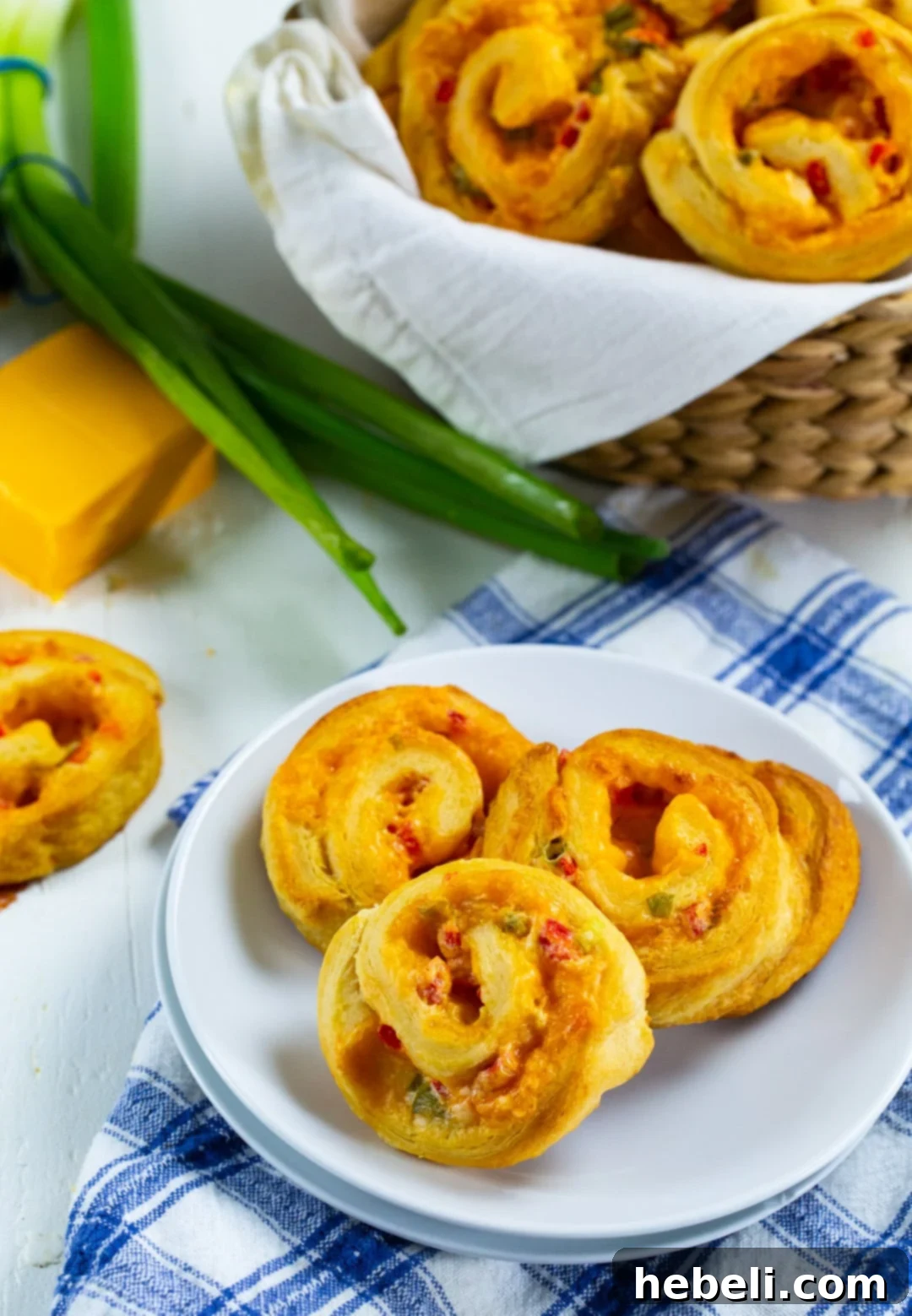 A basket full of baked Pimiento Cheese Spirals next to a plate with more spirals, inviting a closer look.