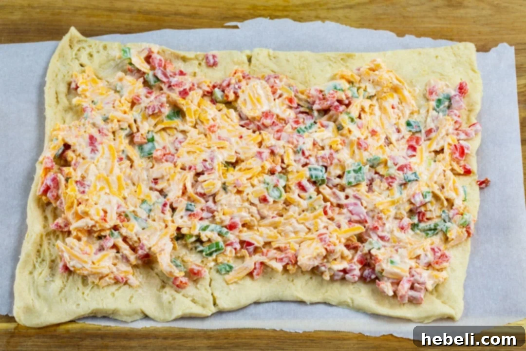 Pimiento cheese spread evenly applied on a flattened sheet of crescent dough before rolling.
