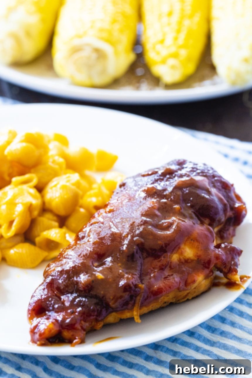 A single BBQ Chicken Breast on a plate with mac and cheese and corn in the background, a complete meal.